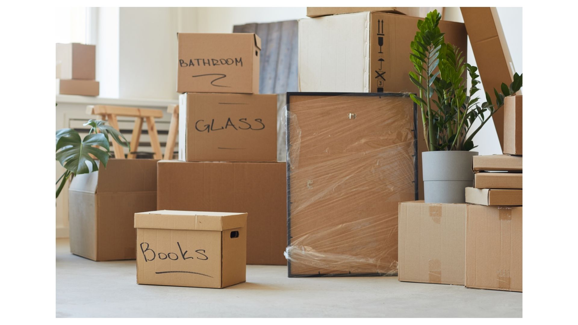 Stacked moving boxes labeled Bathroom, Glass, and Books with wrapped framed art in a San Antonio home