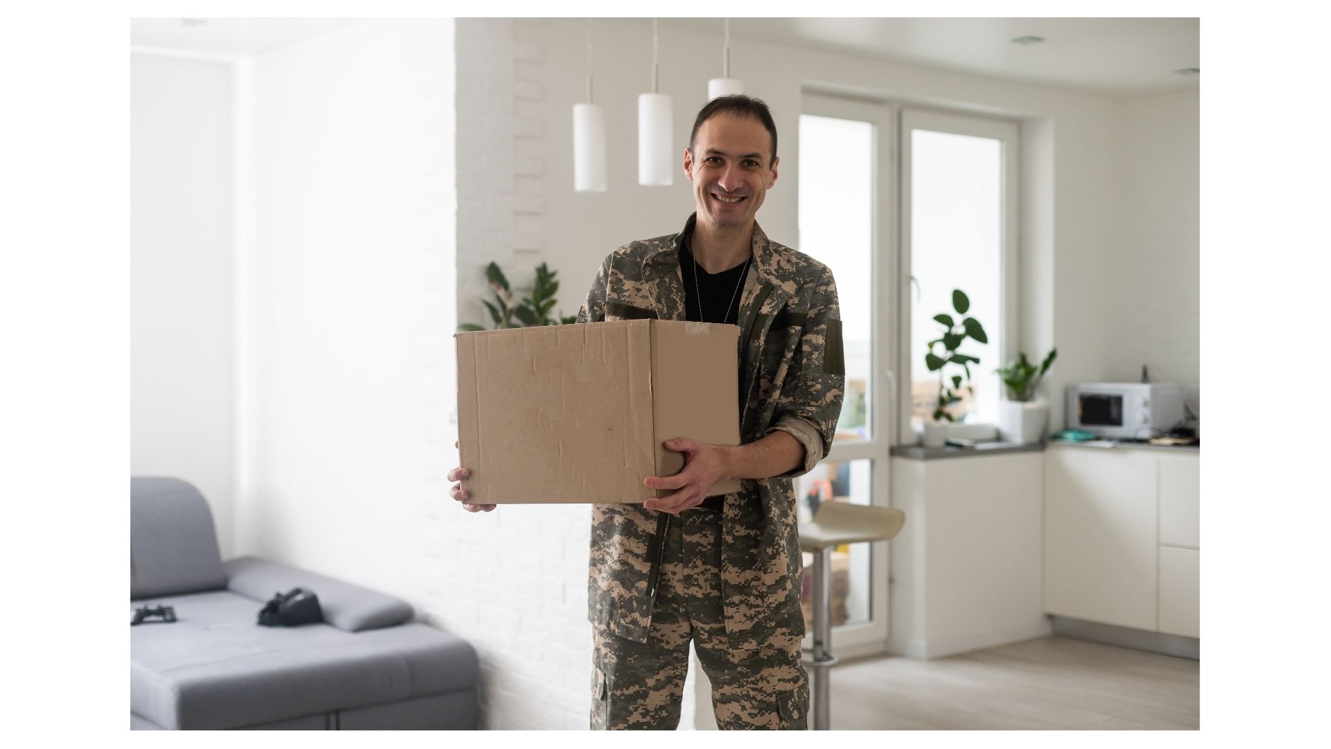 Smiling service member in camouflage uniform carrying a moving box into a Corpus Christi home